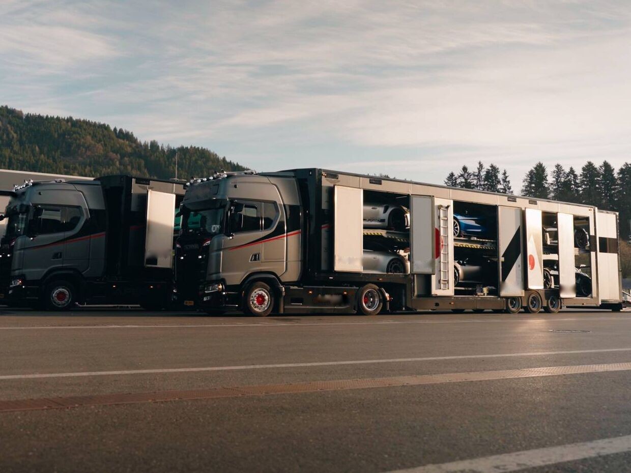 Geschlossene Autotransporter mit geöffneten Seitentüren, beladen mit Sportwagen, auf einem Rennstreckengelände