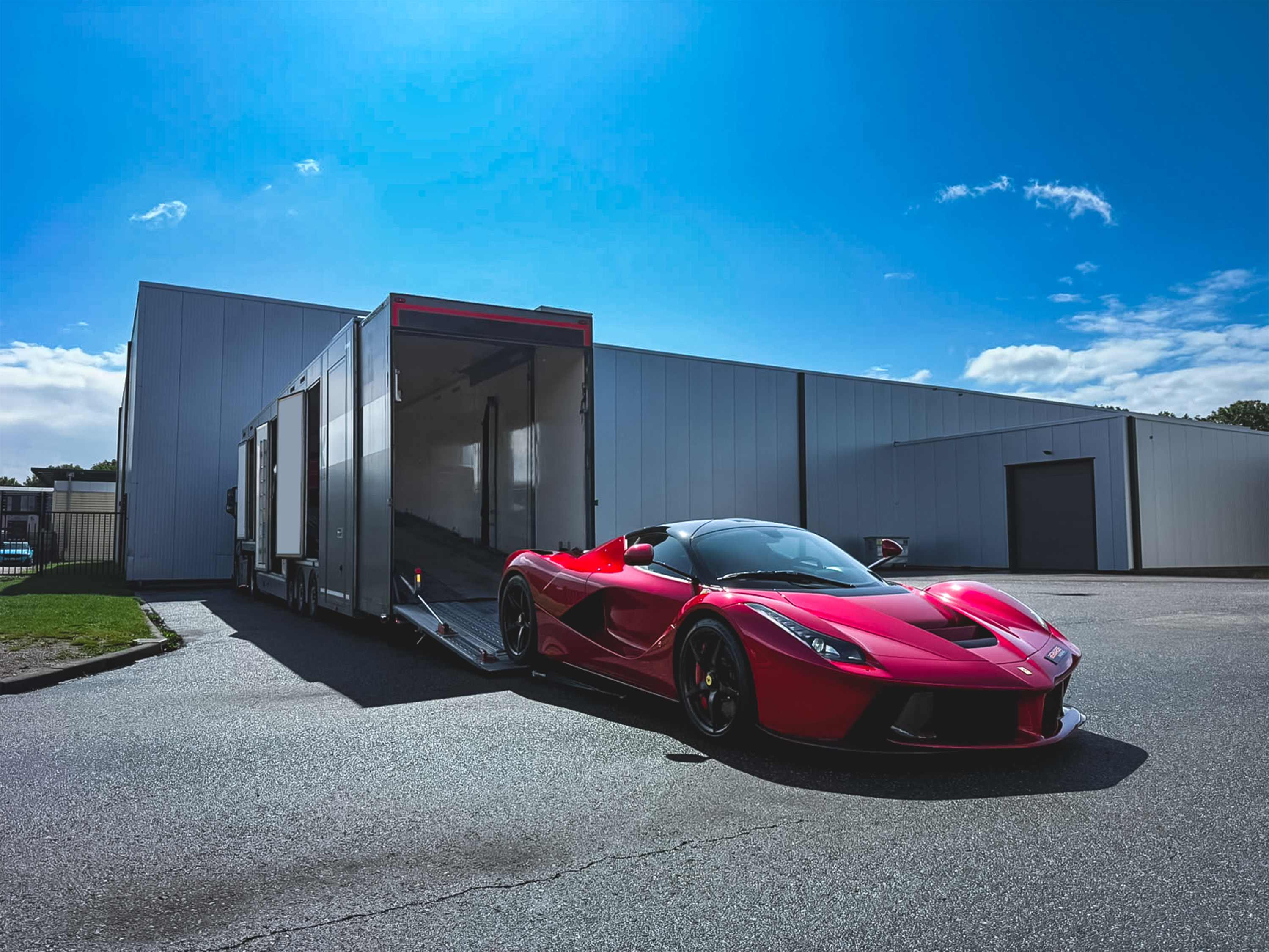 Roter Supersportwagen neben einem geöffneten geschlossenen Autotransporter